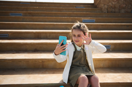 Confident portrait of happy child girl in casual clothes, talking via video link, making selfie,...