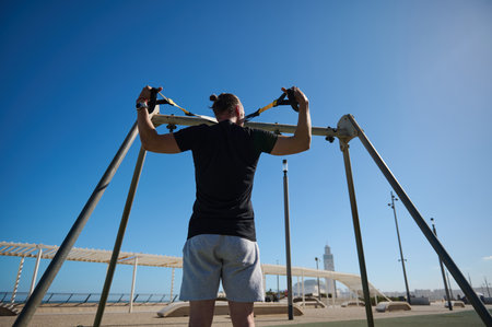 Rear view of a young attractive athletic man doing upper body exercise training arms, using...