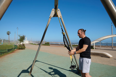 Caucasian determined athlete, young adult sportsman hanging suspension straps on a crossbar, ready...