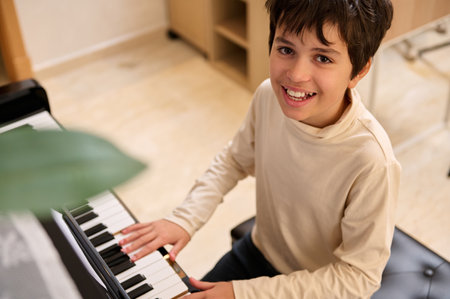 View from above of a Middle Eastern handsome smiling teenage boy, playing grand piano during music lesson at homeの写真素材