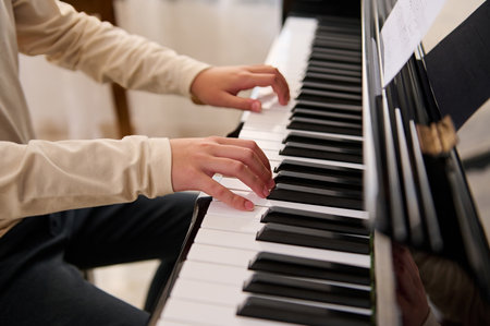 Close-up of a child boy touching piano keys with fingers, performs a musical composition while playing grand piano. Lesson of music.の写真素材