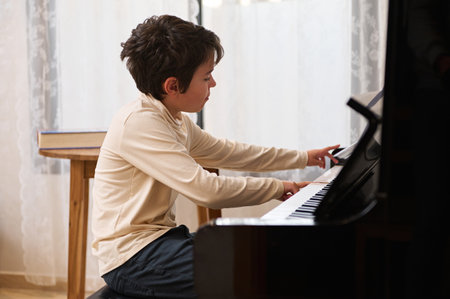 Caucasian elementary age schoolboy touching white and black keys, performing classical musical...