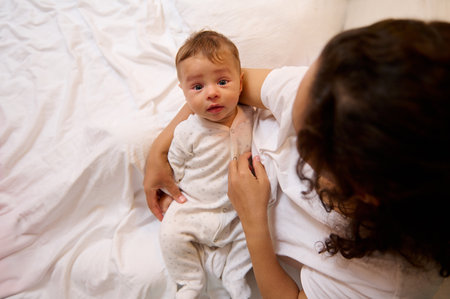 Portrait of authentic little baby boy in the hands of his mother, sitting together on the bed in...
