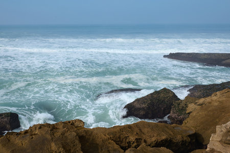 Beautiful waves making white sea foam while pounding on rocks and cliff of the Atlantic ocean shore. Clean clear blue sky on the horizon. Copy advertising space. Nature background. Landscapeの写真素材
