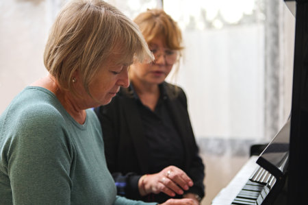 Portrait of two diverse mature women playing piano together at home. Music as therapy.の写真素材