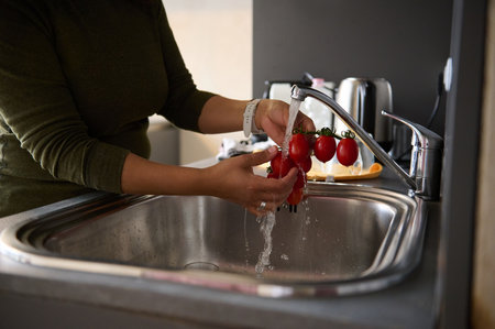 Close-up of a woman housewife washing ripe organic tomato cherry under a tap with running water, in the home kitchenの写真素材