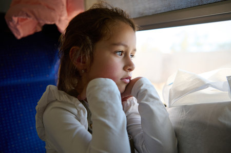 Close-up portrait of a Caucasian pensive beautiful little child girl dreamily looking out the train...