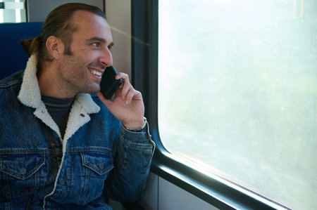 Close-up portrait of a handsome young man commuter smiling talking on smart mobile phone and looking...
