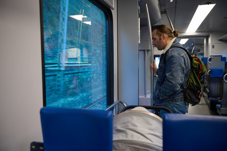 Young adult handsome Caucasian man tourist with backpack, riding train, standing at exit door, ready to disembarking on railway station. The concept of trip and travel using railroad public transportの写真素材