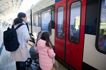 Rear view of a mom and daughter, boarding embarking a high-speed train on the platform of a railway station, and travel from city to another using railroad public urban transport. People. Lifestyleの写真素材