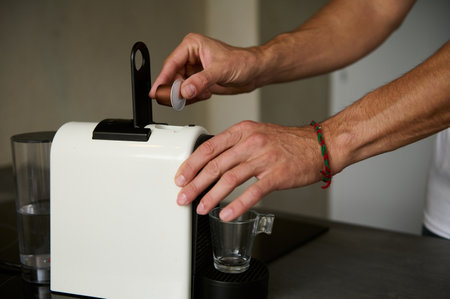 Close-up male hand prepares espresso coffee for breakfast in the morning, inserting a capsule with...