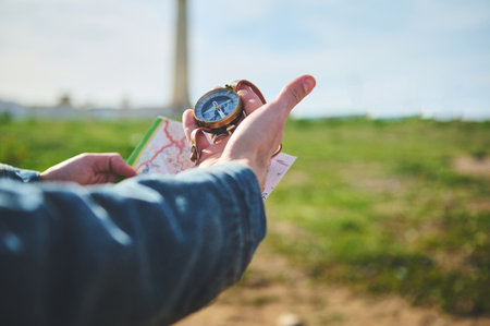 Close-up hands of a male hiker tourist traveler looking for directions with a compass, standing on the beach against a lighthouse background. People and travel. Active lifestyle. Adventure conceptの写真素材
