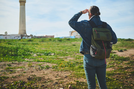 Rear view of a traveler hiker man with backpack, standing back to the camera and looking into the distance, standing over a lighthouse background on a foggy day. People. Travel and active lifestyleの写真素材