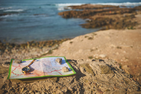 Still life with a golden compass on a geographic map lying down on the top of a rock overlooking...