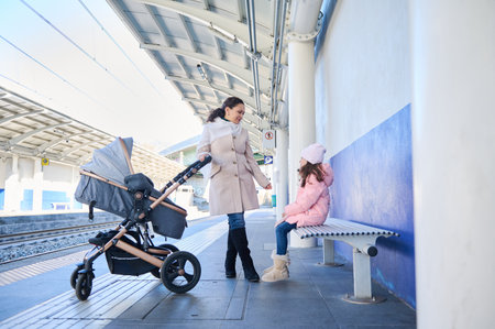 Full length portrait of a mother with children waiting train on the railway station platform. Pretty...
