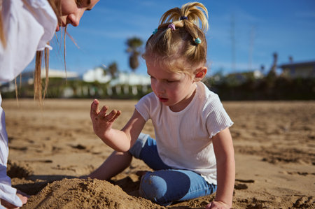Little girl building sandy castle on the beach. Mother and daughter playing together outdoorの写真素材