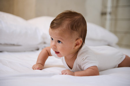 Close-up portrait of Caucasian adorable lovely baby boy in white bodysuit during tummy time on the...