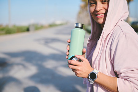 Selective focus on a green stainless steel bottle with refreshing isotonic water, in the hands of a...
