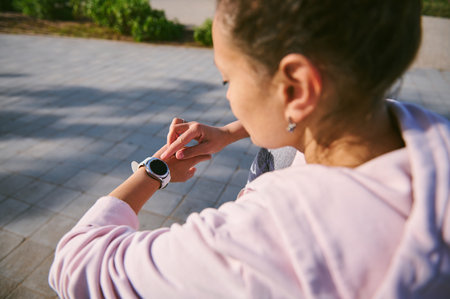 Overhead view of sportswoman checking mobile app on her wrist watch. Close-up rear view of athlete woman setting up the smartwatch for running outdoor. People. Active healthy lifestyle. Sport conceptの写真素材