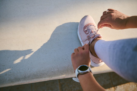 Top view female athlete, sportswoman tying laces on pink sneakers, wearing smart wristwatch on hand...