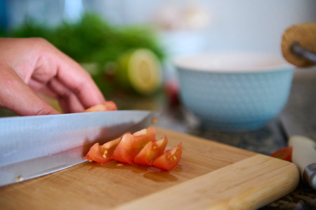 Cropped view of a chef cook slicing red juicy tomatoes on a wooden cutting board. Food background....