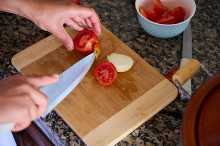 Top view of chef's hands using a kitchen knife, cutting fresh ripe organic tomatoes on a wooden board. Cook prepares a healthy saladの写真素材