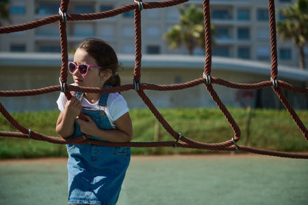 Adorable preschooler girl having fun in adventure park. Caucasian cute little child 6 years old in casual denim, on tree top net trampoline. Active healthy lifestyle. Outdoor activities for small kidsの写真素材