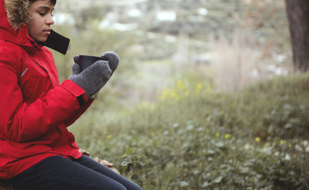 Close-up view of teenage boy in red parka and warm woolen mittens, holding a mug with hot drink,...