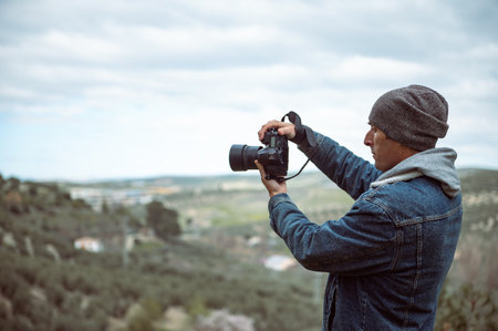 Man photographer capturing beautiful view of mountains on professional camera. Handsome young adult...