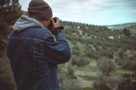 Rear view male travel photographer capturing beautiful of the mountains om his professional digital...