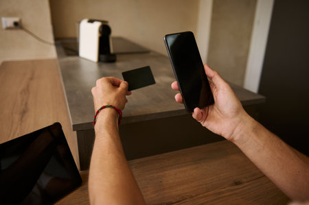 Close-up male hands holding blank black credit card and smartphone with empty mockup digital screen,...