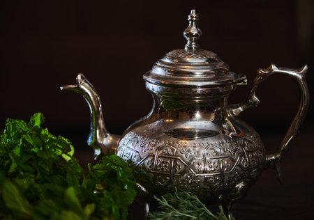 A silver teapot and a bunch of fresh green mint on the foreground. Traditional Moroccan tea as symbol of the hospitality of Moroccan people. Selective focus. Moroccan tea a la mentheの写真素材