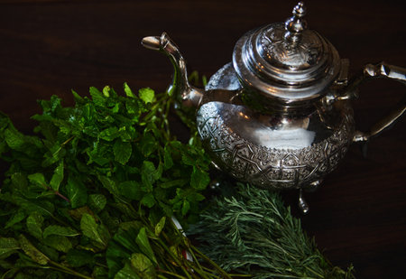 A silver teapot and a bunch of fresh green mint on the foreground. Traditional Moroccan tea as symbol of the hospitality of Moroccan people. Selective focus. Moroccan tea a la menthe. Overhead viewの写真素材
