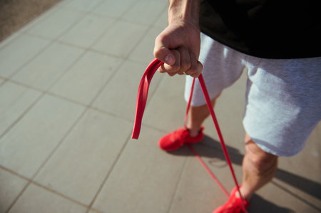 Top view of a sportsman in red sneakers, gray sports shorts and black t-shirt doing warm up exercises with resistance band. Athletic man exercising outdoor with fitness band. Sport and people conceptの写真素材