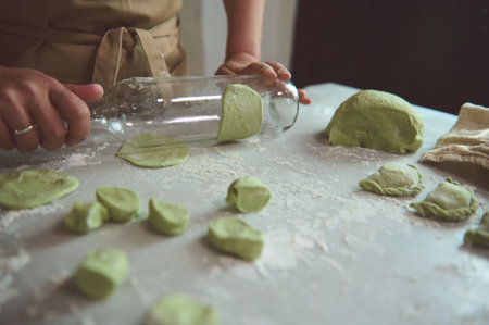 Close-up hands of woman in beige apron, using a glass wine bottle for rolling out the dough with green spinach, cooking traditional Ukrainian Varennyky with mashed potatoes. Food. Traditions. Cultureの写真素材