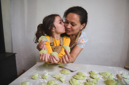 Mom and daughter have fun while cooking dumpling together. Kid girl kissing her mother, happy to...