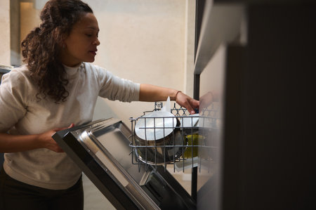 Charming multi ethnic woman loading, unloading, emptying out, putting dishes inside baskets in...