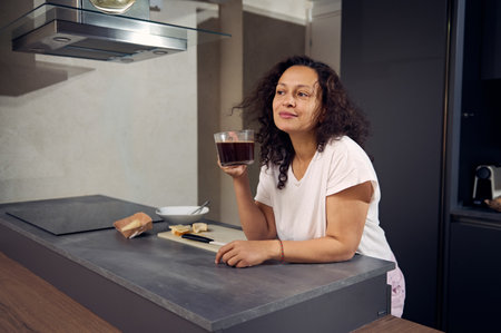 Curly haired brunette holding a cup of coffee, smiling and dreamily thoughtfully looking away,...