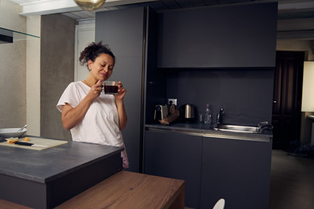 Young woman smiling whole drinking coffee in the home kitchenの写真素材
