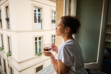 Happy woman admiring the view of a beautiful city overlooked from her house, standing at window with a cup of rom coffee in the sunny morning. Pretty tourist drinks coffee and admire the Como cityの写真素材