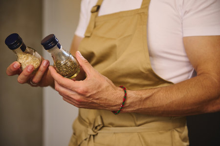 Close-up chef hands holding two glass bottles with condiments, dried basil leaves and ail for...