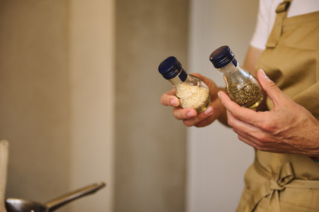 Close-up chef hands holding two glass bottles with condiments for seasoning dish while cooking dinnerの写真素材