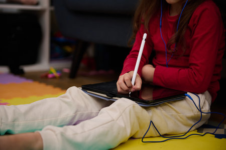 Close-up a white stylus with digital tablet in hands of little child girl learning online, doing...