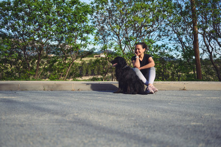 Full size portrait of woman sitting on the parapet, smiling and talking to her dog while taking her pet for a walk on the nature. People and animals conceptの写真素材