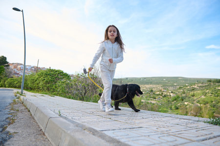 Happy child girl enjoying walking her dog outdoors in the nature. Pretty kid taking her pedigree black cocker spaniel dog for a walk on sunny dayの写真素材