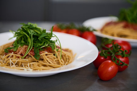 Italian spaghetti capellini with tomato sauce, parmesan cheese and arugula leaves. A branch of fresh ripe organic tomato cherry on the kitchen table.の写真素材