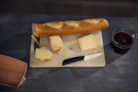 Still life top view breakfast on the kitchen table. A cup of freshly brewed espresso coffee near a cutting board with a whole grain baguette, loaf of bread and sliced cheese on the kitchen tableの写真素材