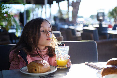 Young girl drinking orange juice and enjoying breakfast at an outdoor cafの写真素材