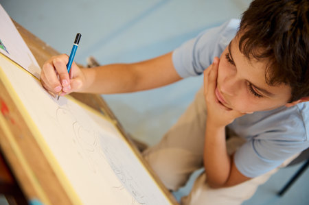Young boy attentively drawing in art class. Focused on his sketch, he shows creativity and...