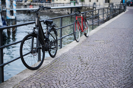 A serene scene with two bicycles parked along a cobblestone path near a river. The metal railing and waterway add to the picturesque urban setting.の写真素材